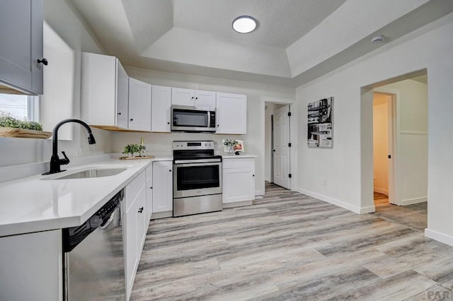 kitchen featuring white cabinets, appliances with stainless steel finishes, light countertops, and a sink