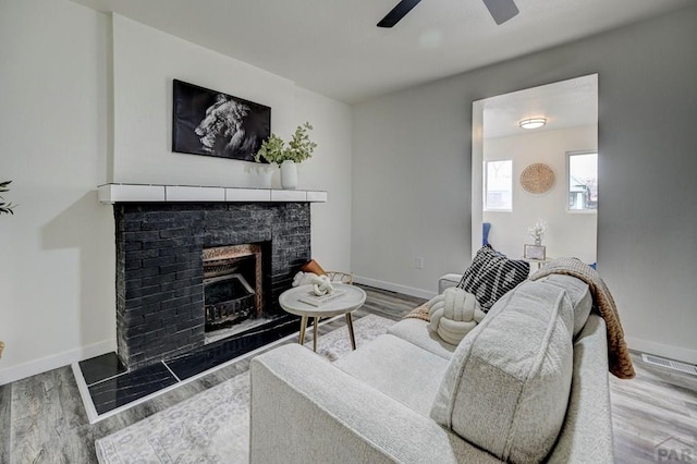 living room featuring a ceiling fan, a fireplace, baseboards, and wood finished floors