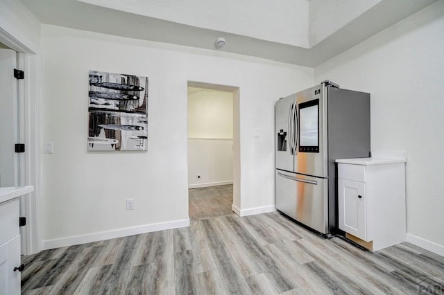 kitchen featuring baseboards, stainless steel fridge with ice dispenser, light countertops, light wood-type flooring, and white cabinetry