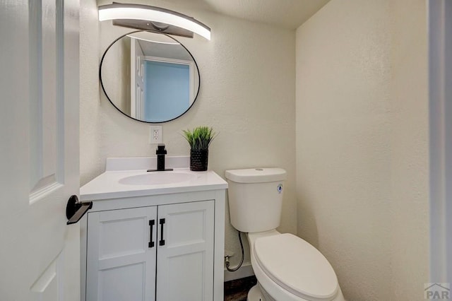 half bath featuring toilet, a textured wall, and vanity