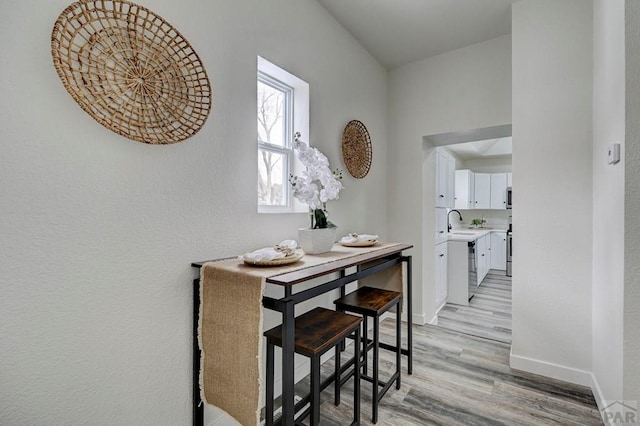 hallway with light wood-type flooring, a sink, and baseboards