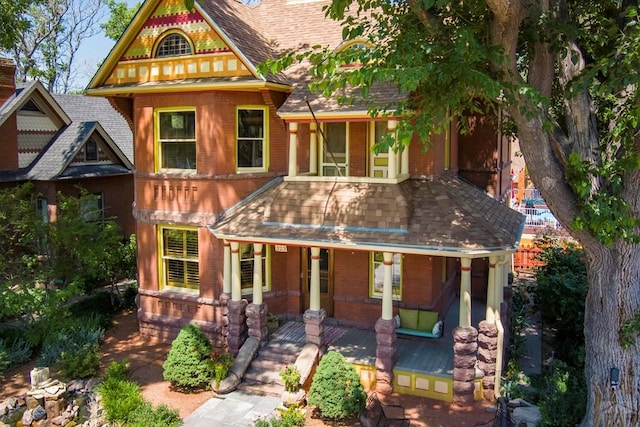 victorian home featuring a porch, brick siding, and a shingled roof