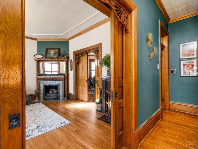 corridor with baseboards, ornamental molding, and light wood-style floors