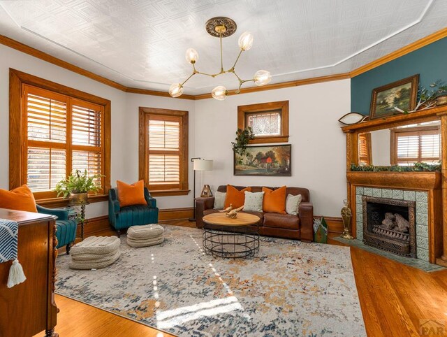 living room with baseboards, wood finished floors, an inviting chandelier, crown molding, and a fireplace