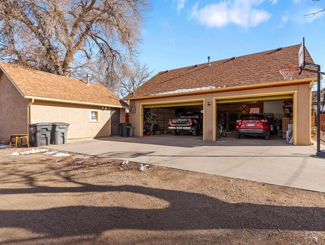 exterior space with a shingled roof, a detached garage, and stucco siding