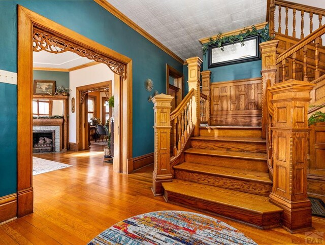 stairs featuring an ornate ceiling, a fireplace, ornamental molding, and wood finished floors