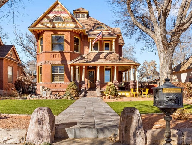 victorian home featuring covered porch, brick siding, and a front yard