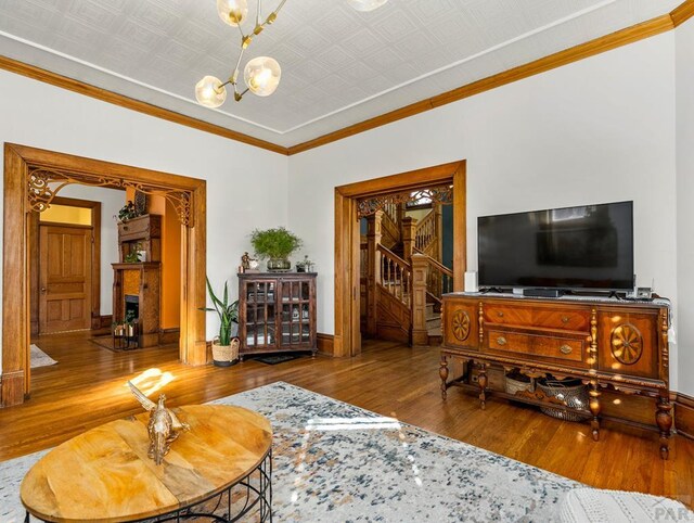 living area with an ornate ceiling, a fireplace, an inviting chandelier, wood finished floors, and stairs