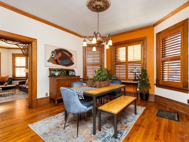 dining room with a notable chandelier, visible vents, ornamental molding, wood finished floors, and baseboards