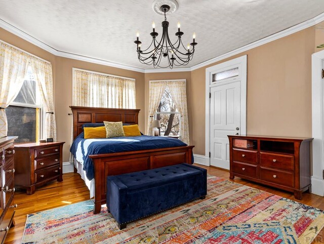 bedroom with light wood-style floors, baseboards, a chandelier, and crown molding