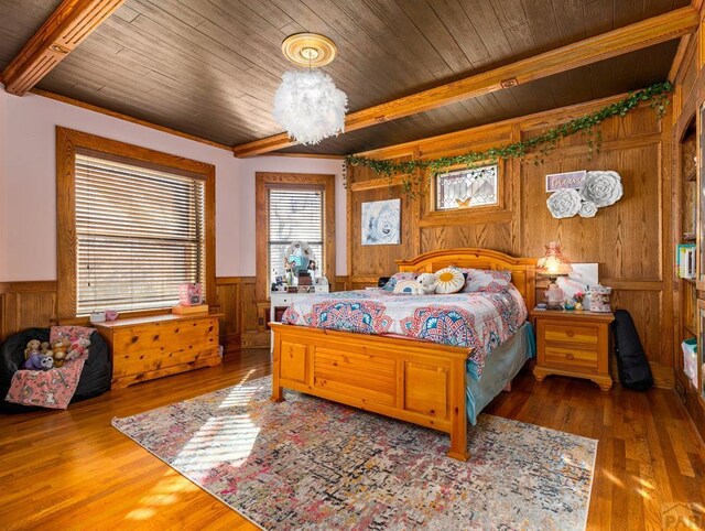 bedroom with wooden ceiling, a wainscoted wall, beam ceiling, and wood finished floors