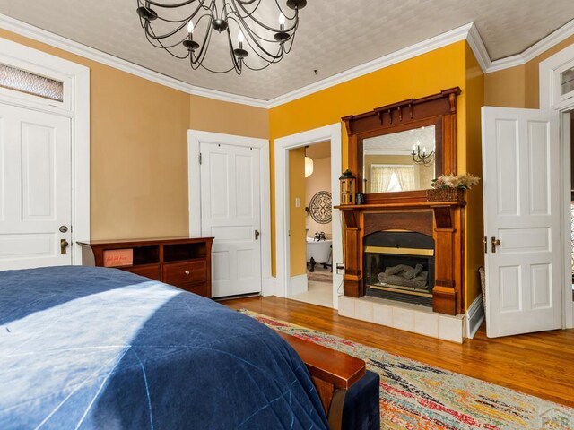 bedroom with an inviting chandelier, ornamental molding, wood finished floors, and a glass covered fireplace