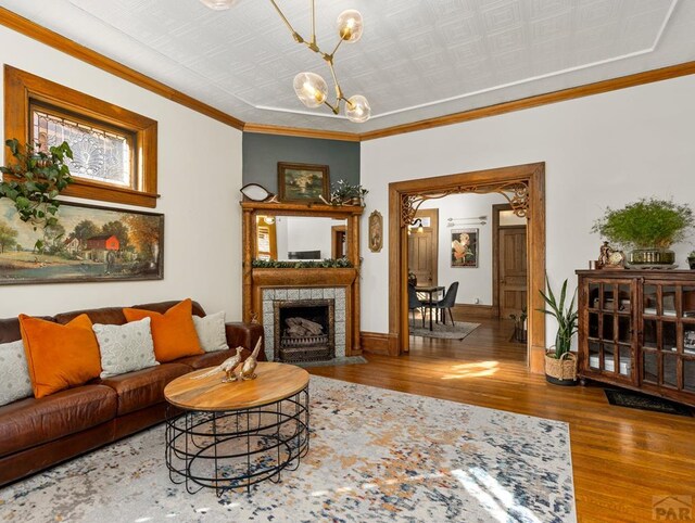 living area featuring wood finished floors, an inviting chandelier, baseboards, a tiled fireplace, and crown molding