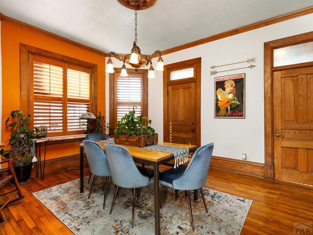 dining space with ornamental molding, a notable chandelier, baseboards, and wood finished floors