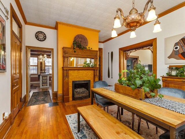 interior space with a notable chandelier, a fireplace, wood finished floors, baseboards, and ornamental molding