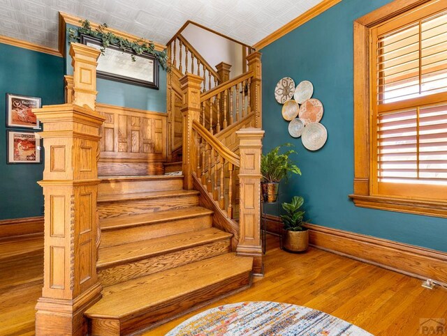 stairs with an ornate ceiling, crown molding, baseboards, wood finished floors, and ornate columns