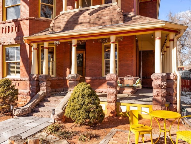 doorway to property with a shingled roof, covered porch, and brick siding