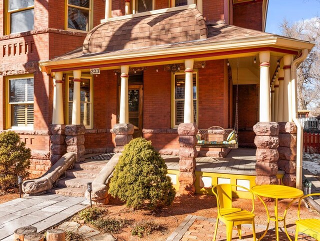 doorway to property with a shingled roof, covered porch, and brick siding