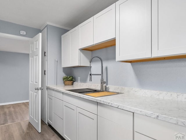 kitchen featuring light stone counters, white cabinetry, and a sink