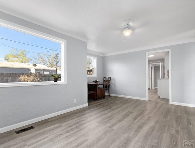 interior space with a ceiling fan, visible vents, light wood-style flooring, and baseboards