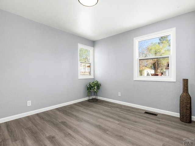 spare room with baseboards, visible vents, and wood finished floors