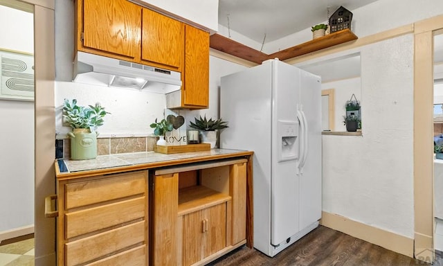 kitchen featuring dark wood-style flooring, light countertops, white fridge with ice dispenser, under cabinet range hood, and baseboards