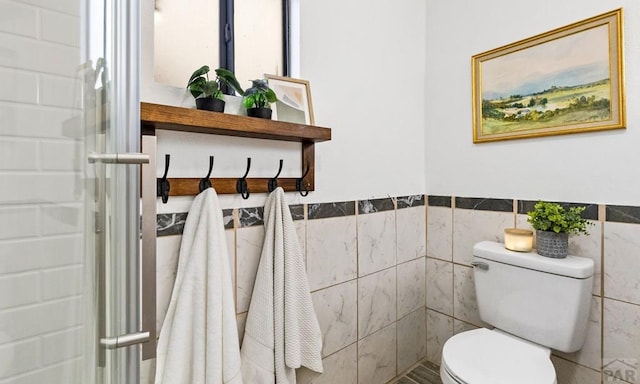 full bath featuring toilet, a shower with shower door, tile walls, and wainscoting