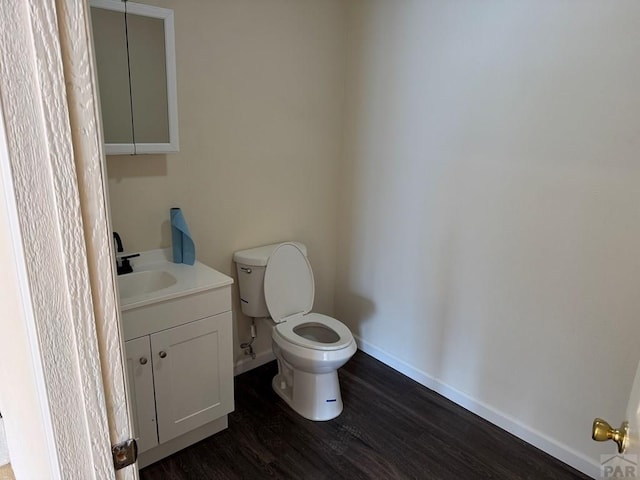 half bathroom with baseboards, vanity, toilet, and wood finished floors