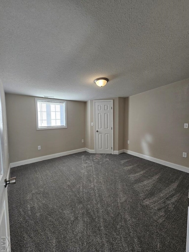 empty room featuring a textured ceiling, dark carpet, and baseboards