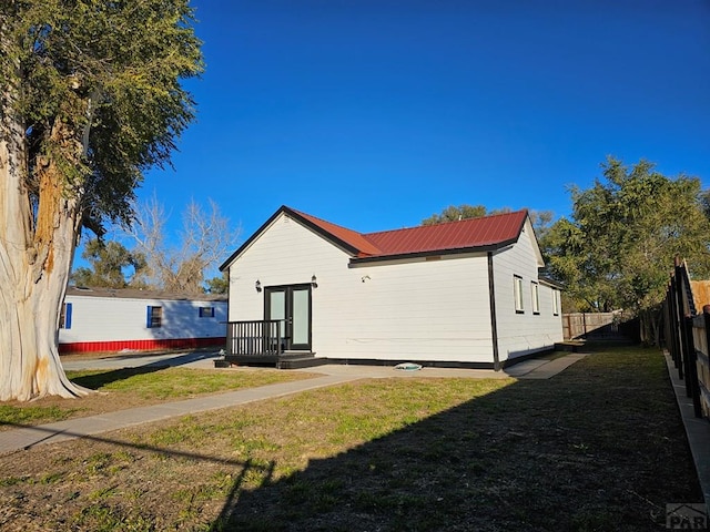 back of house with metal roof, fence, and a lawn