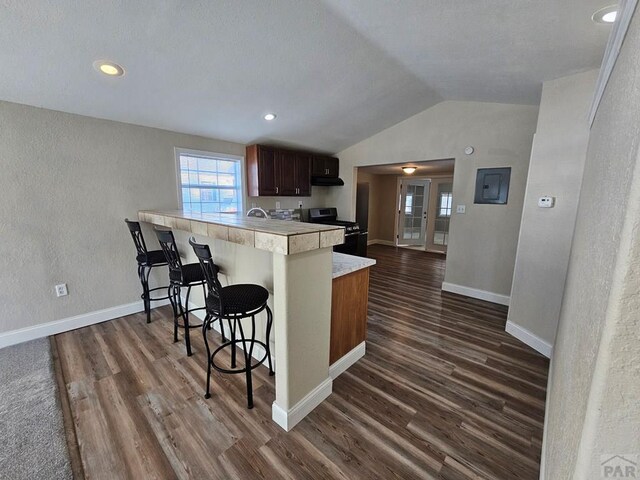 kitchen with dark wood-style flooring, stainless steel electric range oven, a breakfast bar area, light countertops, and a peninsula