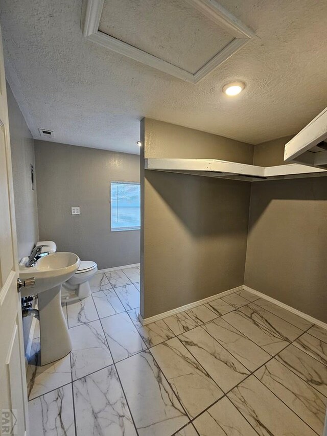 half bathroom with a textured ceiling, toilet, visible vents, baseboards, and marble finish floor