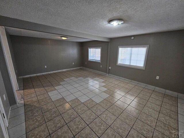 spare room featuring light tile patterned floors, baseboards, and a textured ceiling