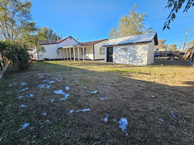 rear view of house featuring an outbuilding, metal roof, a yard, and fence