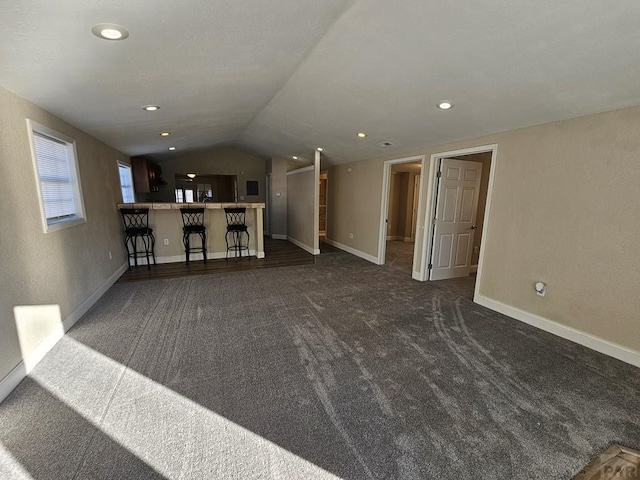 unfurnished living room featuring vaulted ceiling, recessed lighting, dark carpet, and baseboards