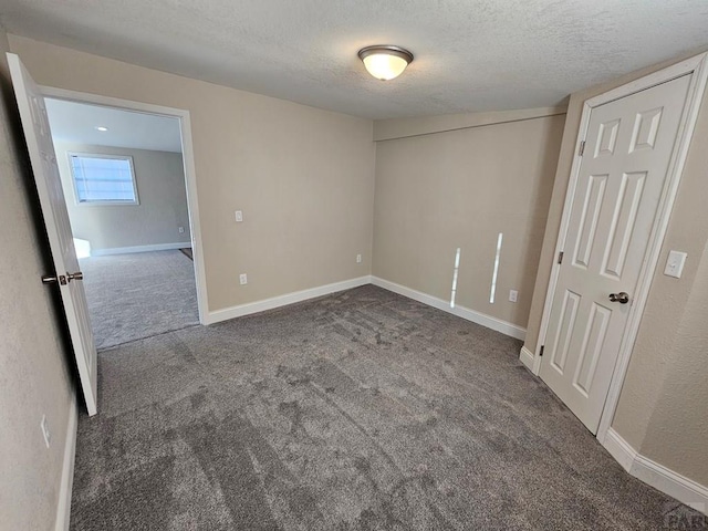 spare room with a textured ceiling, dark carpet, and baseboards