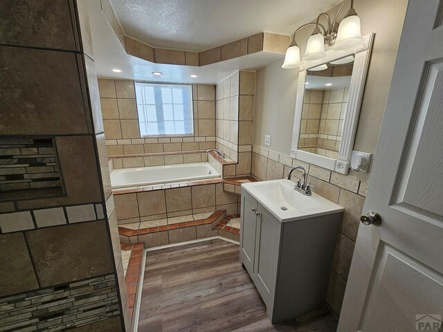 bathroom with a garden tub, tile walls, vanity, and wood finished floors