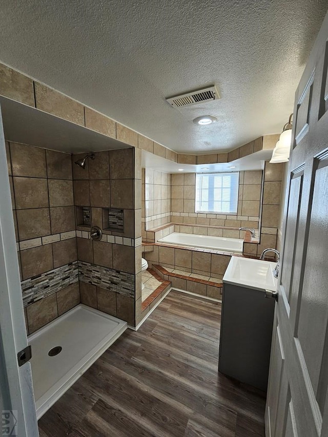 full bathroom with visible vents, vanity, a textured ceiling, wood finished floors, and tiled shower