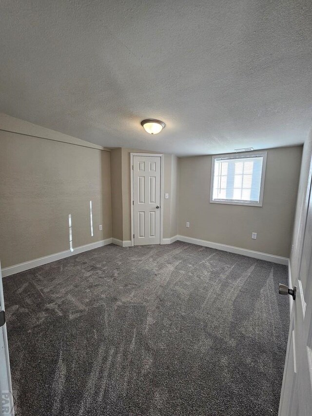 empty room featuring baseboards, dark carpet, and a textured ceiling