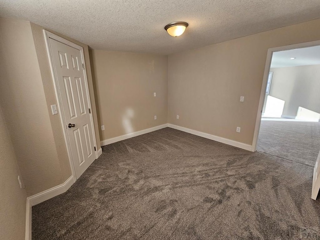 spare room with a textured ceiling, dark carpet, and baseboards