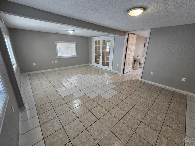 spare room with a textured ceiling, french doors, light tile patterned flooring, and baseboards