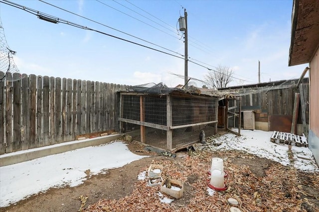 snowy yard featuring an outbuilding, fence, and exterior structure