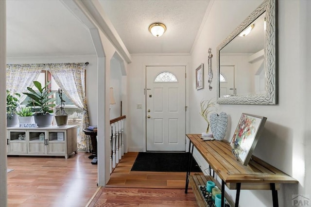 entrance foyer with a textured ceiling, ornamental molding, wood finished floors, and a healthy amount of sunlight