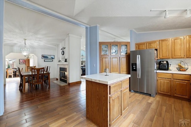 kitchen with pendant lighting, stainless steel refrigerator with ice dispenser, lofted ceiling, light countertops, and a kitchen island