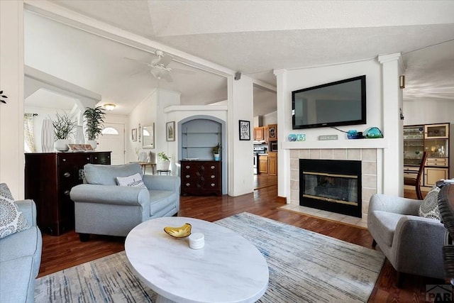 living area featuring vaulted ceiling with beams, ceiling fan, dark wood-type flooring, and a fireplace