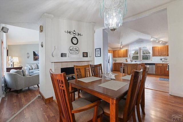 dining space with an inviting chandelier, a tiled fireplace, vaulted ceiling, and wood finished floors