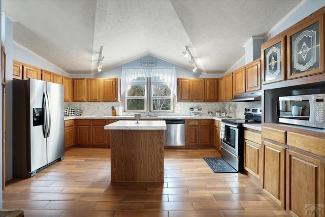 kitchen featuring brown cabinets, a center island, stainless steel appliances, light countertops, and under cabinet range hood