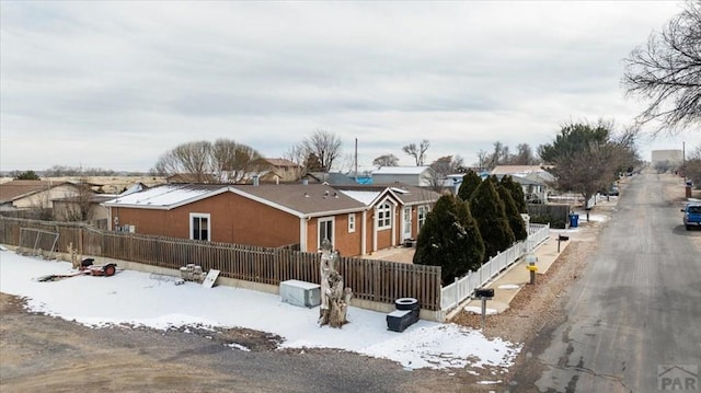 snow covered rear of property featuring a fenced front yard, a residential view, and stucco siding