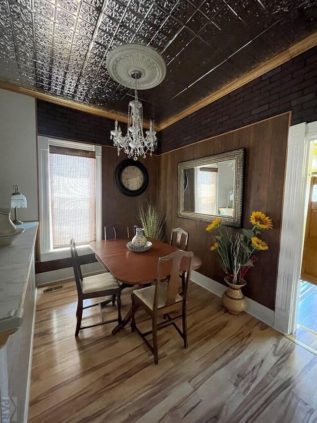 dining room with brick wall, wood finished floors, an ornate ceiling, and a notable chandelier