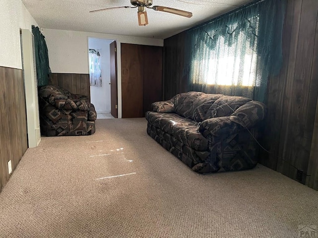 carpeted living room with a textured ceiling, wood walls, wainscoting, and a ceiling fan